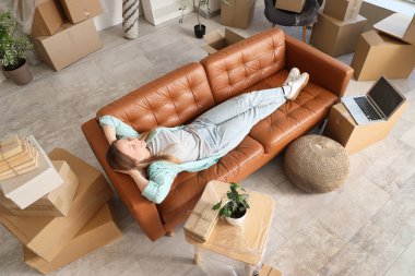 Genç bir kadın yeni dairesinde kanepede uzanıyor.