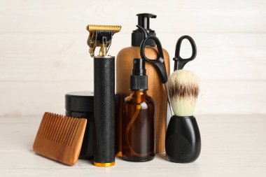 Makas, kozmetik ürünleri şişeleri ve beyaz ahşap arka planda fırçalarla modern budayıcı.