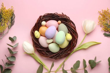 Paskalya yumurtaları, yuvası, yeşil dalları ve pembe arka planda çiçekleri olan kompozisyon