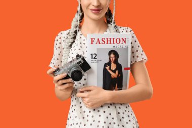 Güzel, genç, şık, mutlu bir kadın. Dergi ve fotoğraf makinesiyle turuncu arka planda. Yakın plan.