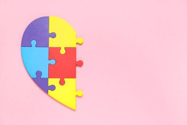 Pembe arka planda kalp şeklinde renkli yapboz parçaları. Otistik bozukluk kavramı
