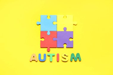Sarı arka planda renkli yapboz parçaları olan kelime AUTISM. Otistik bozukluk kavramı