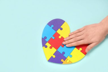 Mavi arka planda kalp şeklinde renkli yapboz parçaları olan bir kadın eli. Otistik bozukluk kavramı