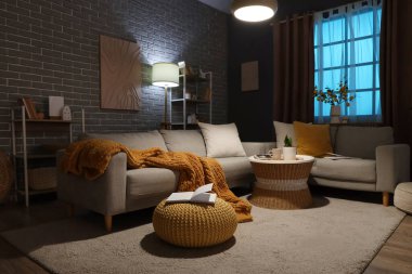 Konforlu kanepe, parlayan lamba ve oturma odasında perdeleri olan pencere.