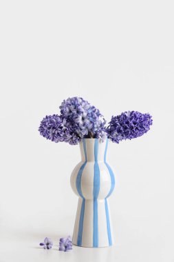 Beyaz arka planda güzel mor sümbül çiçekleri olan vazo.