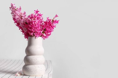 Beyaz duvarın yanındaki masada, üzerinde pembe sümbül çiçekleri olan vazo.