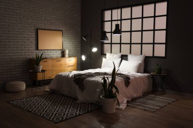 Geceleri rahat yatağı ve parlak lambaları olan modern yatak odasının içinde.