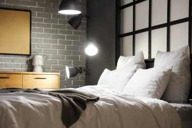 Geceleri modern yatak odasında rahat yatak ve parlak lambalar.