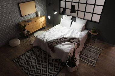 Geceleri rahat yatağı ve parlak lambaları olan modern yatak odasının içinde.