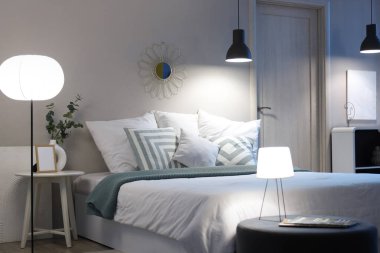 Geceleri rahat yatağı, çiçekleri ve parlayan lambaları olan modern yatak odasının içinde.