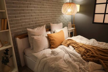 Geceleri modern yatak odasında buruşuk battaniyeli, parlak lambalı rahat bir yatak.