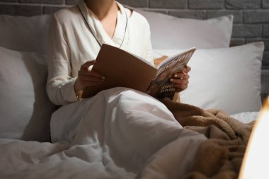 Geceleri rahat bir yatakta kitap okuyan genç bir kadın.