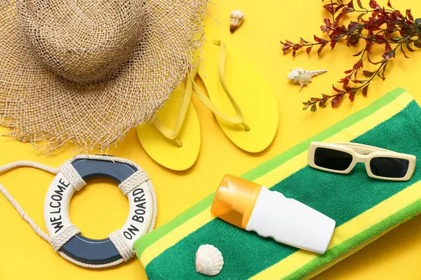Can simidi halkalı hasır şapka, güneş kremi, havlu ve sarı arka planda parmak arası terlik. Yaz konsepti