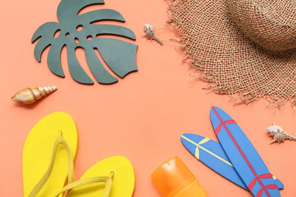 Parmak arası terlikli mini sörf tahtaları, güneş kremi ve turuncu arka planda hasır şapka. Yaz konsepti