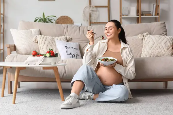 Genç hamile kadın evde sebze salatası yiyor.