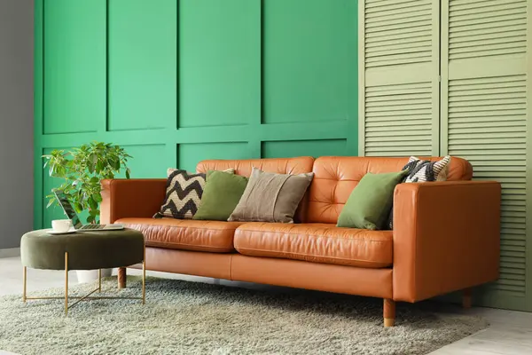 Oturma odasının içinde şık bir deri kanepe, katlanabilir ekran ve yeşil duvarın yanındaki bir laptopta.