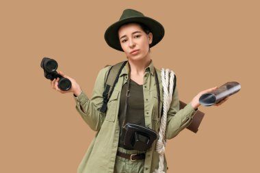 Bej arka planda silkelenen haritalı ve dürbünlü üzgün genç bayan turist