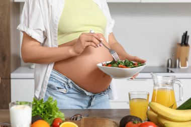 Mutfaktaki masada sebze salatalı genç hamile kadın, yakın plan.