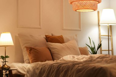 Rahat bir yatak, gece şık bir yatak odasında parıldayan lambalar ve çiçekler.