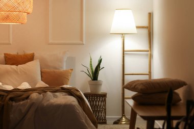 Şık bir yatak odası, rahat bir yatak odası, komodinin yanında çiçek ve gece şık bir yatak odasında parlayan bir lamba.