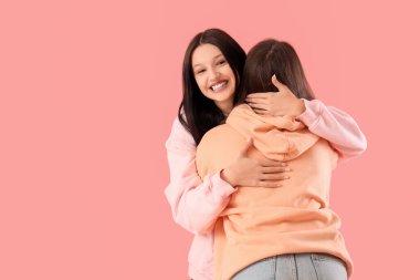 Mutlu genç kızlar pembe arka planda sarılıyorlar.