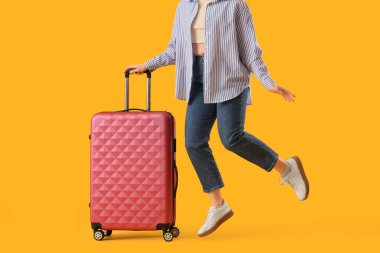 Sarı arka plana atlayan bavullu genç bir kadın, yakın plan. Seyahat kavramı