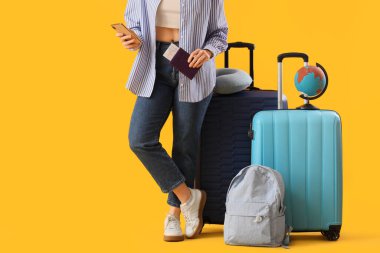 Çantalı genç bir kadın, sırt çantası, pasaport ve cep telefonu sarı arka planda, yakın plan. Seyahat kavramı