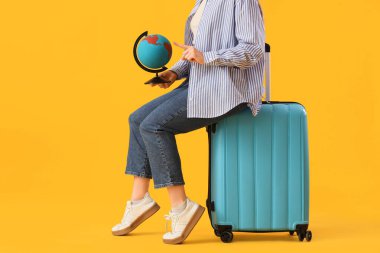 Çantalı genç kadın sarı arka plandaki küreyi işaret ediyor, yakın plan. Seyahat kavramı