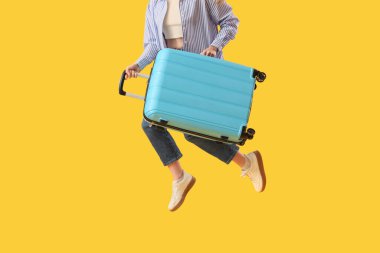 Sarı arka plana atlayan bavullu genç bir kadın, yakın plan. Seyahat kavramı