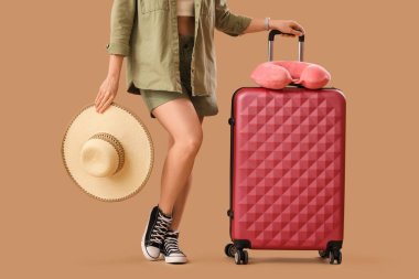 Bavulu, şapkası ve yastığı olan bej arka planda genç bir kadın, yakın plan. Seyahat kavramı