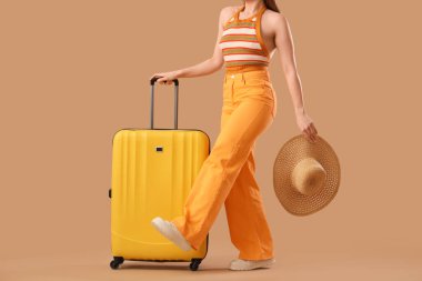 Bavulu ve bej arka planda hasır şapkalı genç bayan, yakın plan. Seyahat kavramı