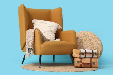 Şık kahverengi koltuk, hasır puf ve mavi arka planda klasik bavullar.