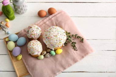 Beyaz ahşap arka planda boyalı yumurta ve okaliptüs dalları olan tatlı Paskalya pastaları.