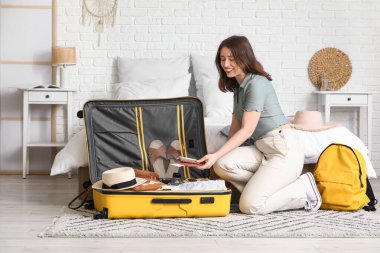 Güzel genç bir kadın, açık otel odasında bavulunu giysileriyle açıyor.