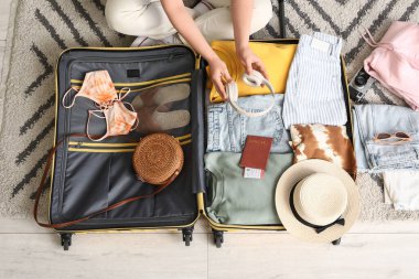 Otel odasında bavulunu elbiseleriyle ve kulaklıklarıyla boşaltan genç bir kadın.