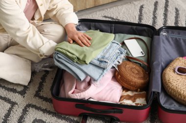 Otel odasında bavulunu elbiseleriyle açan genç bir kadın, yakın plan.