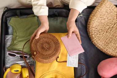 Genç bir kadın otel odasında bavulunu giysileri, pasaportu ve seyahat aksesuarlarıyla boşaltıyor.