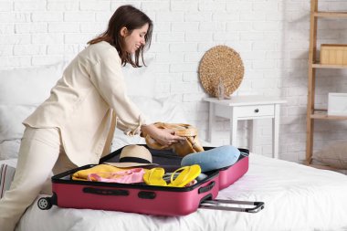 Güzel genç bir kadın, açık otel odasında bavulunu giysileriyle açıyor.