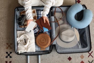 Genç bir kadın bavulunu elbiseleriyle, cep telefonuyla ve cüzdanıyla açıyor.