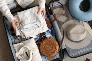 Genç bir kadın bavulunu evde kıyafetleriyle açıyor.