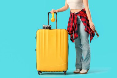 Mavi arka planda güneş gözlüklü ve valizli bir kadın turist.