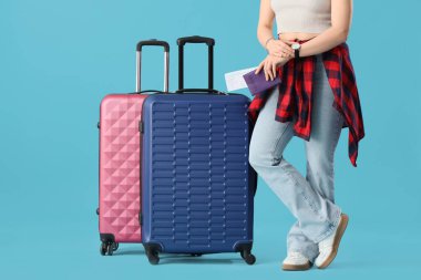 Pasaportlu ve bavullu bir bayan turist mavi arka planda kol saatine bakıyor.