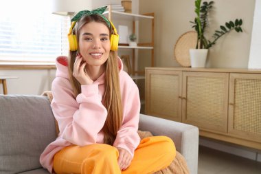 Pembe kapüşonlu, kulaklıklı şık bir kadın evdeki kanepede oturuyor.
