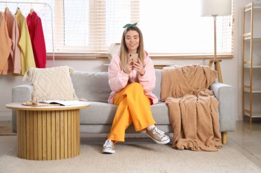 Evdeki kanepede cep telefonu kullanan kapüşonlu şık bir genç kadın.