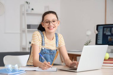 Evde dizüstü bilgisayarı ve bilgisayarı olan genç bir kız çalışıyor.