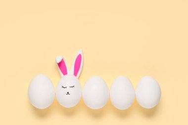 Yüzü çizilmiş Paskalya yumurtaları ve bej arka planda tavşan kulakları