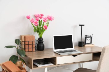 Çalar saati, dizüstü bilgisayarı ve vazoda güzel lale çiçekleri olan modern işyeri.
