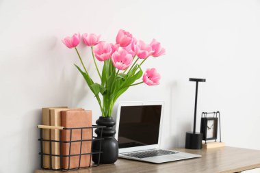 Çalar saati, dizüstü bilgisayarı ve vazoda güzel lale çiçekleri olan modern işyeri.
