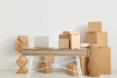 Beyaz duvarın yanındaki masada bir sürü paket ve dizüstü bilgisayar olan bir oda.