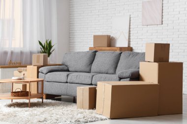 Oturma odasının içinde kanepe, sehpa ve beyaz tuğla duvarın yanında bir sürü paket var.